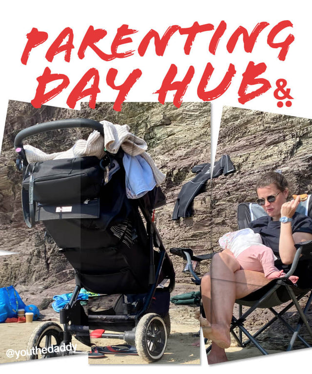 Mom sitting on a chair at the beach feeding baby with a 3 wheel stroller in the foreground - parenting day hub -  philandteds.com